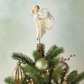 Angel figurine in white dress standing on stand on green tree branches and ornaments