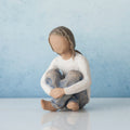 Faceless young girl figurine wearing white shirt and blue jeans sitting with her hands on her knees