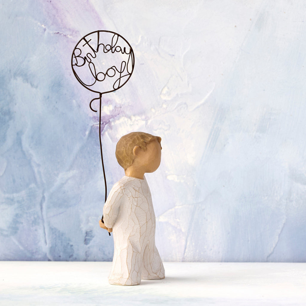 Willow Tree Birthday Boy, 5”h hand-painted standing resin figure in cream onesie, holding wire ballon with 'birthday boy' written in wire, in front of blue painting