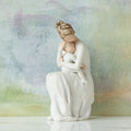 Willow Tree For Always, 6.5”h hand-painted resin female figure, seated, holding toddler on lap, both in cream clothes, arms around each other, in front of blue painting