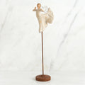 Far shot of angel figurine dressed in white dress dancing with arms and legs out - she is on a brown wooden stand