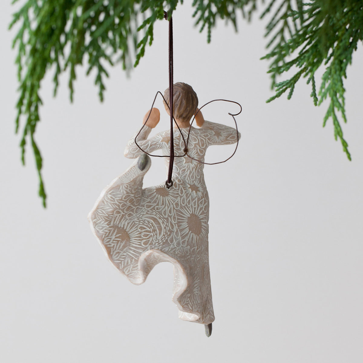 Back view of woman angel figurine ornament in white dress hanging from green tree