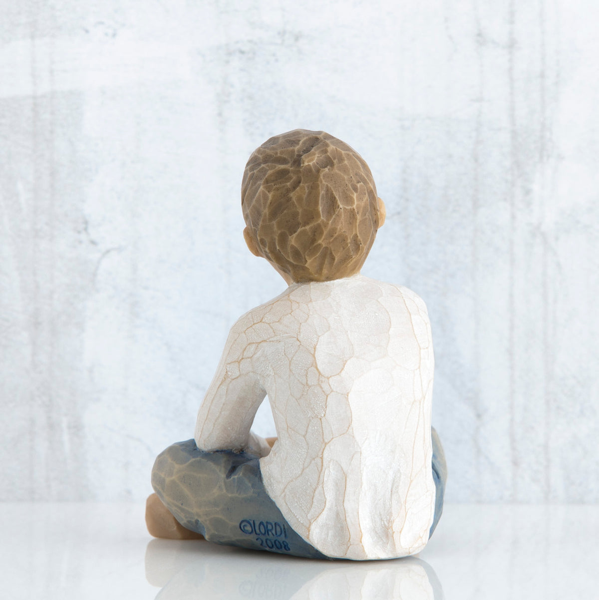 Back view of young brunette boy in white shirt and blue jeans sitting down