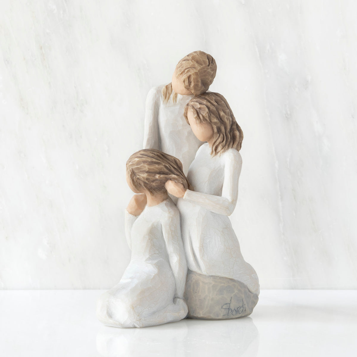 Left-facing view, figurine of three females in cream dresses: one standing with arm around kneeling female, and holding hand of seated female