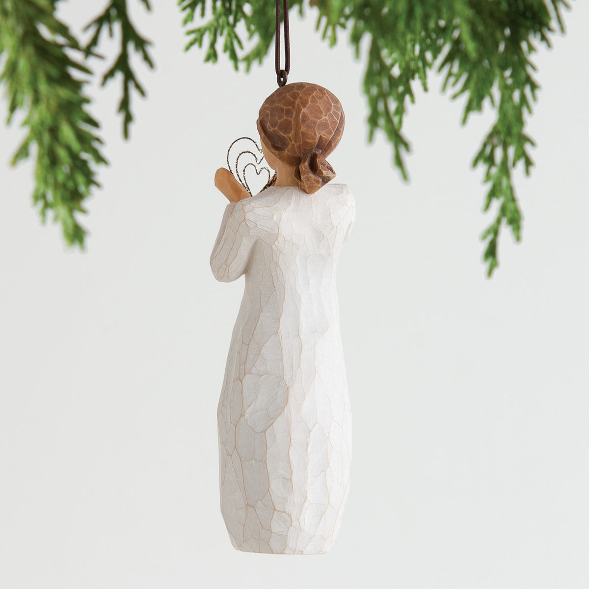 Back view of brunette girl ornament wearing white dress hung from green christmas tree