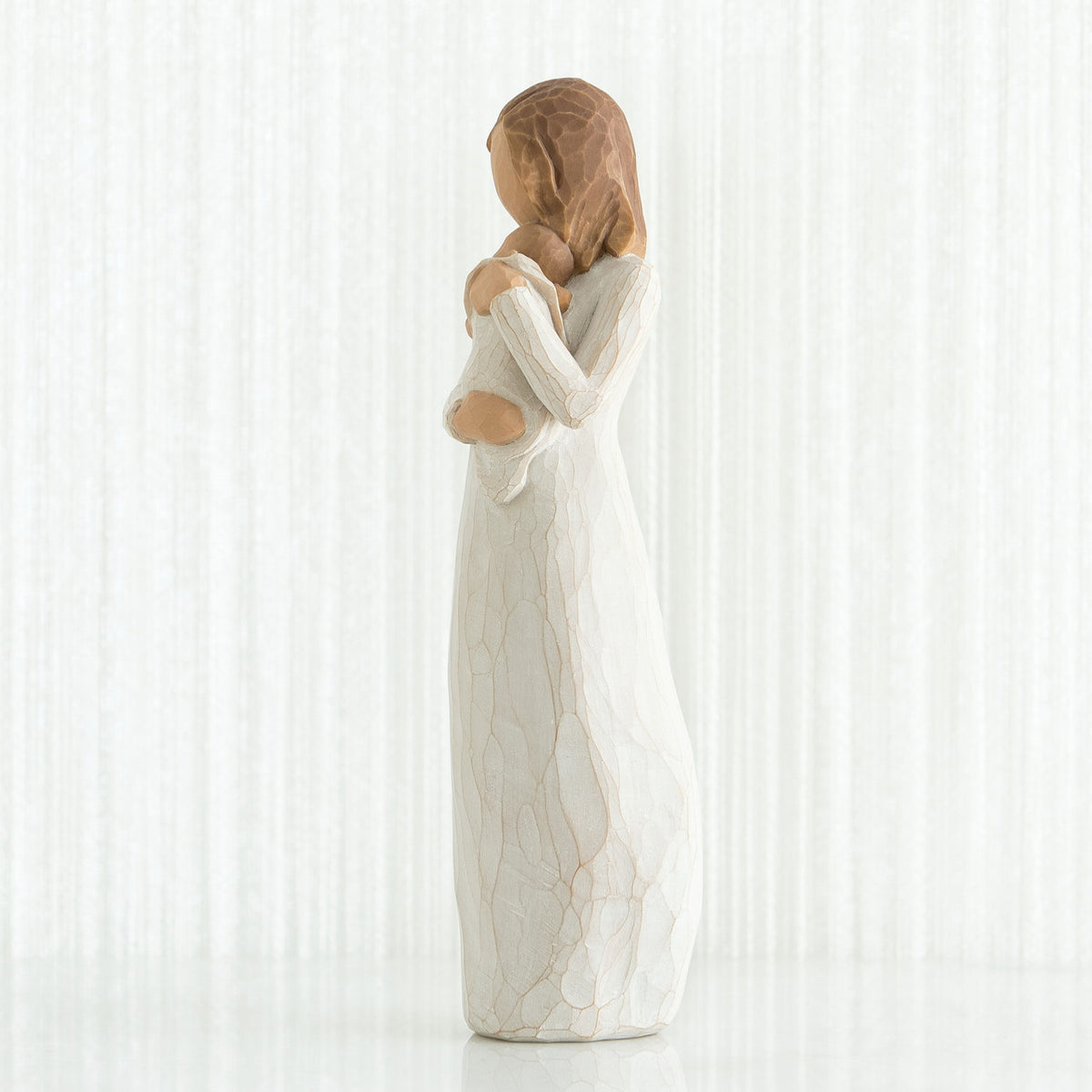 Side view of brunette girl figurine in white dress holding baby