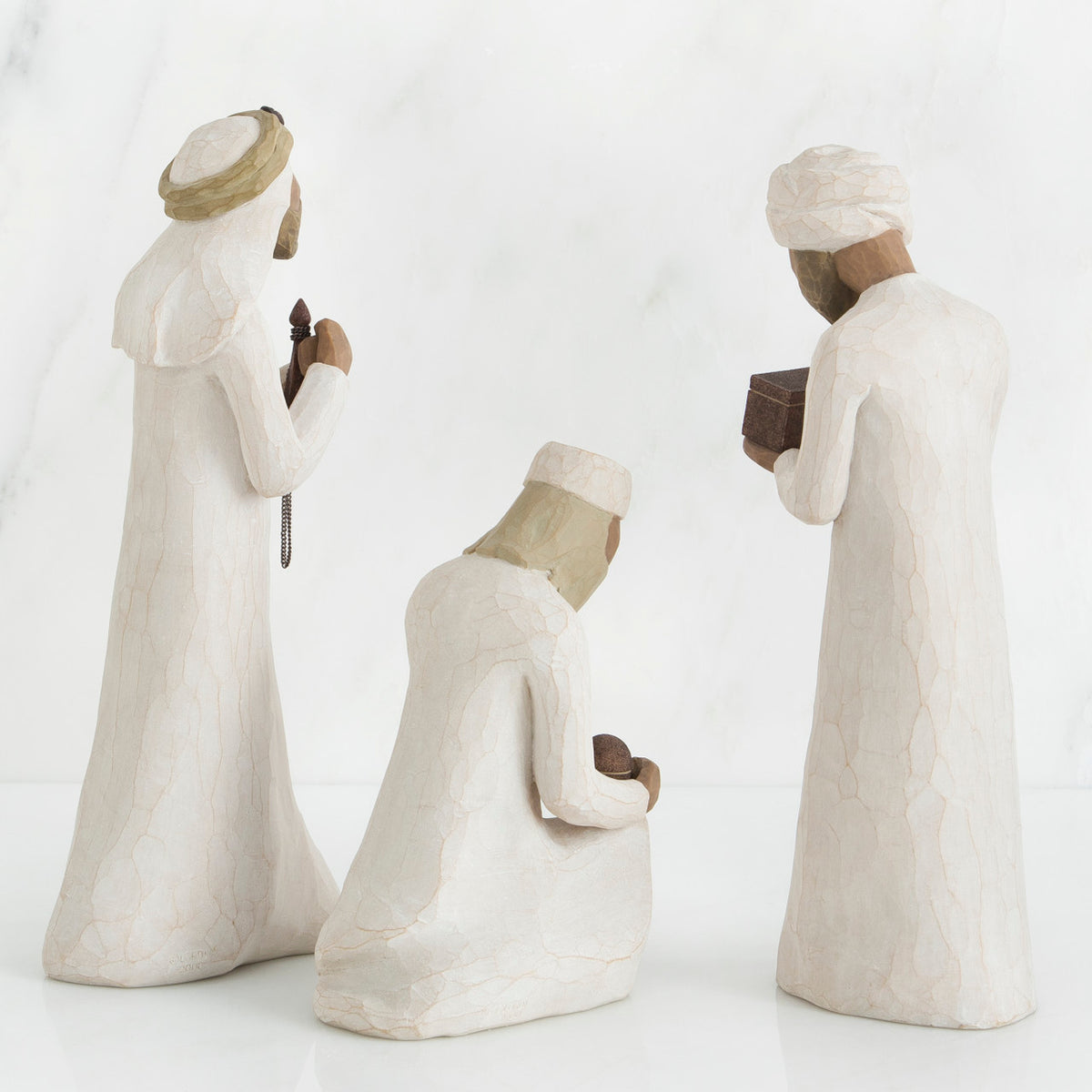 Set of three wiseman figurines in white standing facing the back holding boxes
