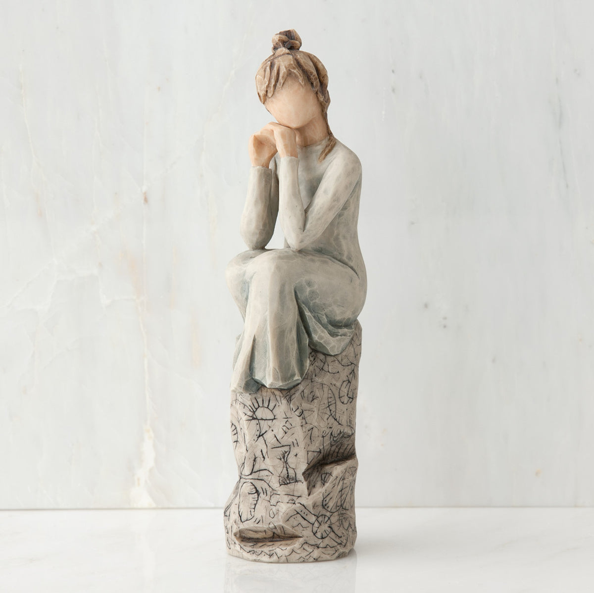 Brunette girl figurine in grey dress sitting on grey rock with her hands to her face