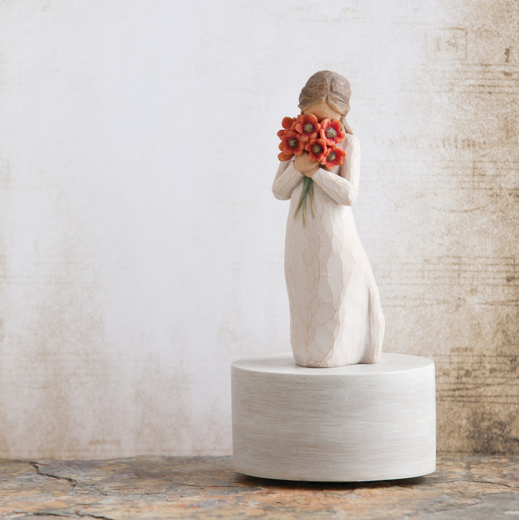 Willow Tree Surrounded by Love Musical, 7.5”h hand-painted resin figure in cream dress holding large bouquet of red-orange poppies up to face, atop round, cream base containing musical element, in front of cream painting