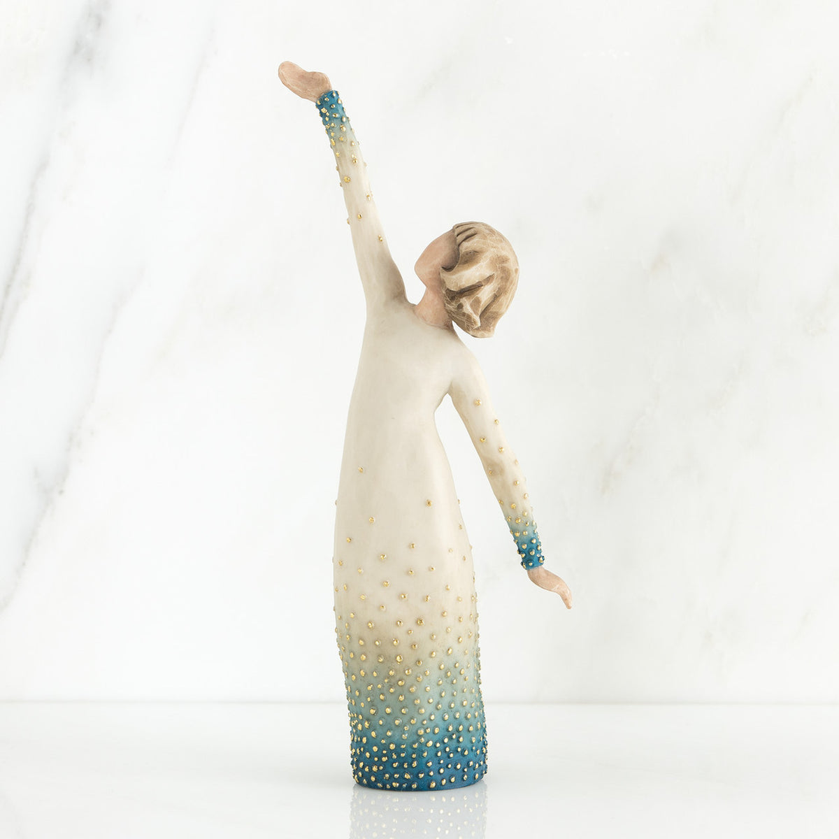 Faceless woman figurine in white dress with blue embellishments - she is facing away from the camera holding both her arms in opposite directions