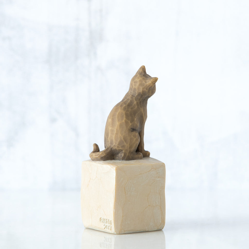 Golden cat figurine facing away sitting on cream square rock