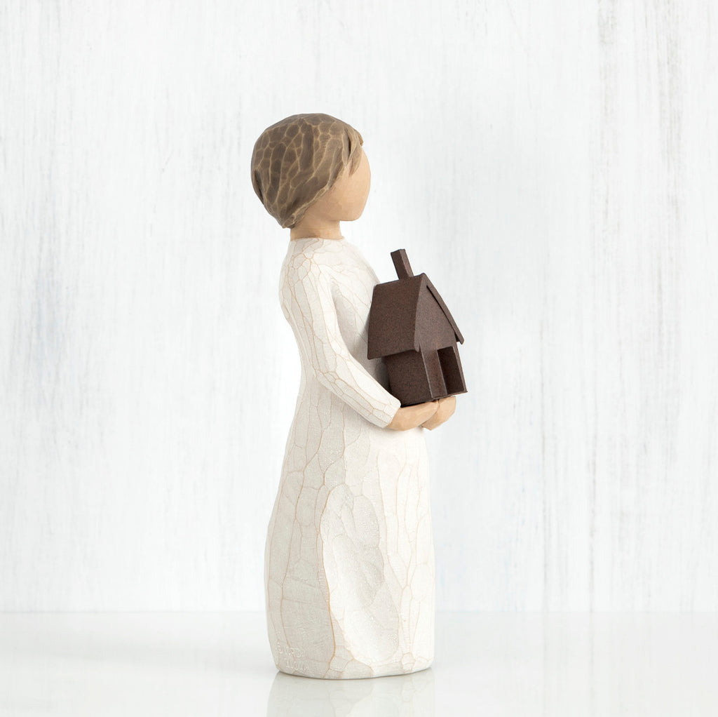 Small brown haired girl figurine in white dress holding brown house figurine