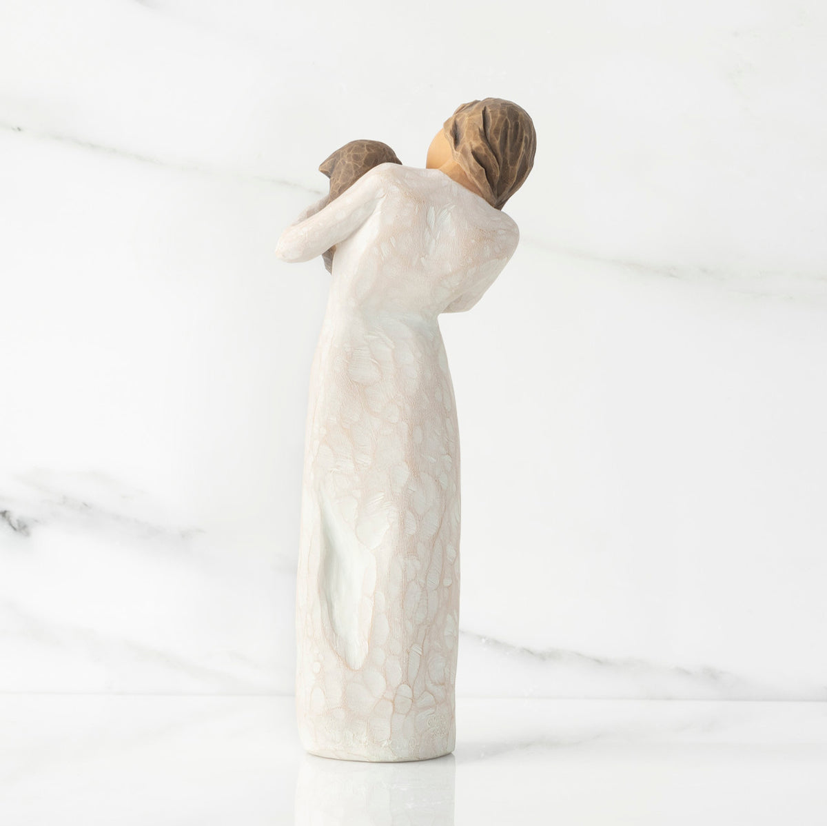 Back view, standing female figure in cream dress, holding dark color puppy in her arms