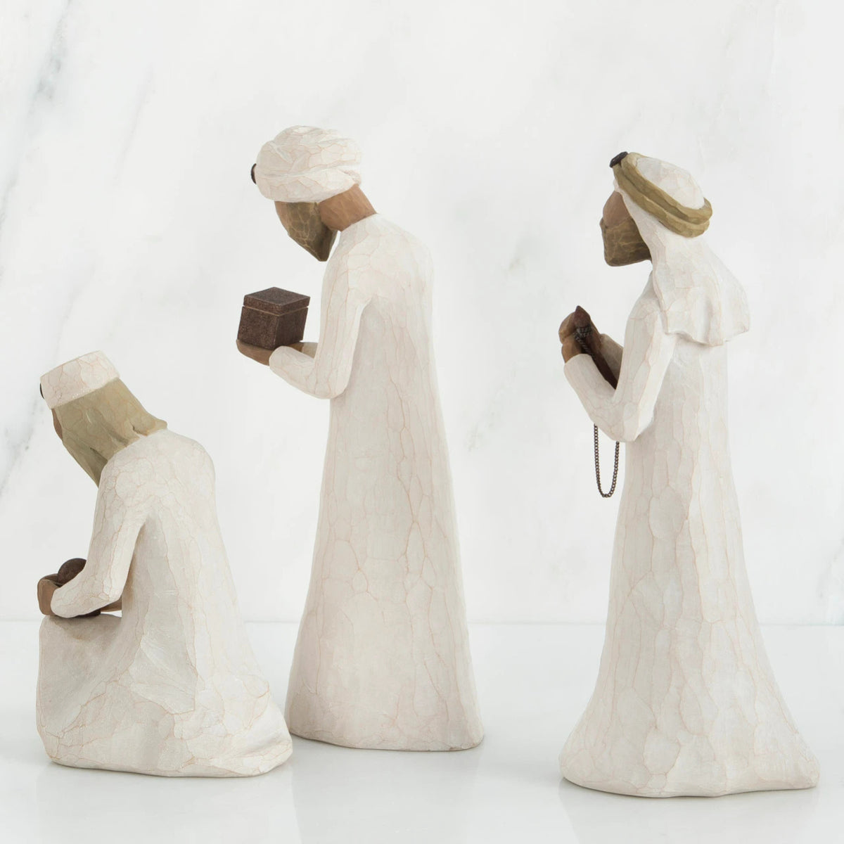Three wiseman figurines in white dresses facing the side holding brown boxes