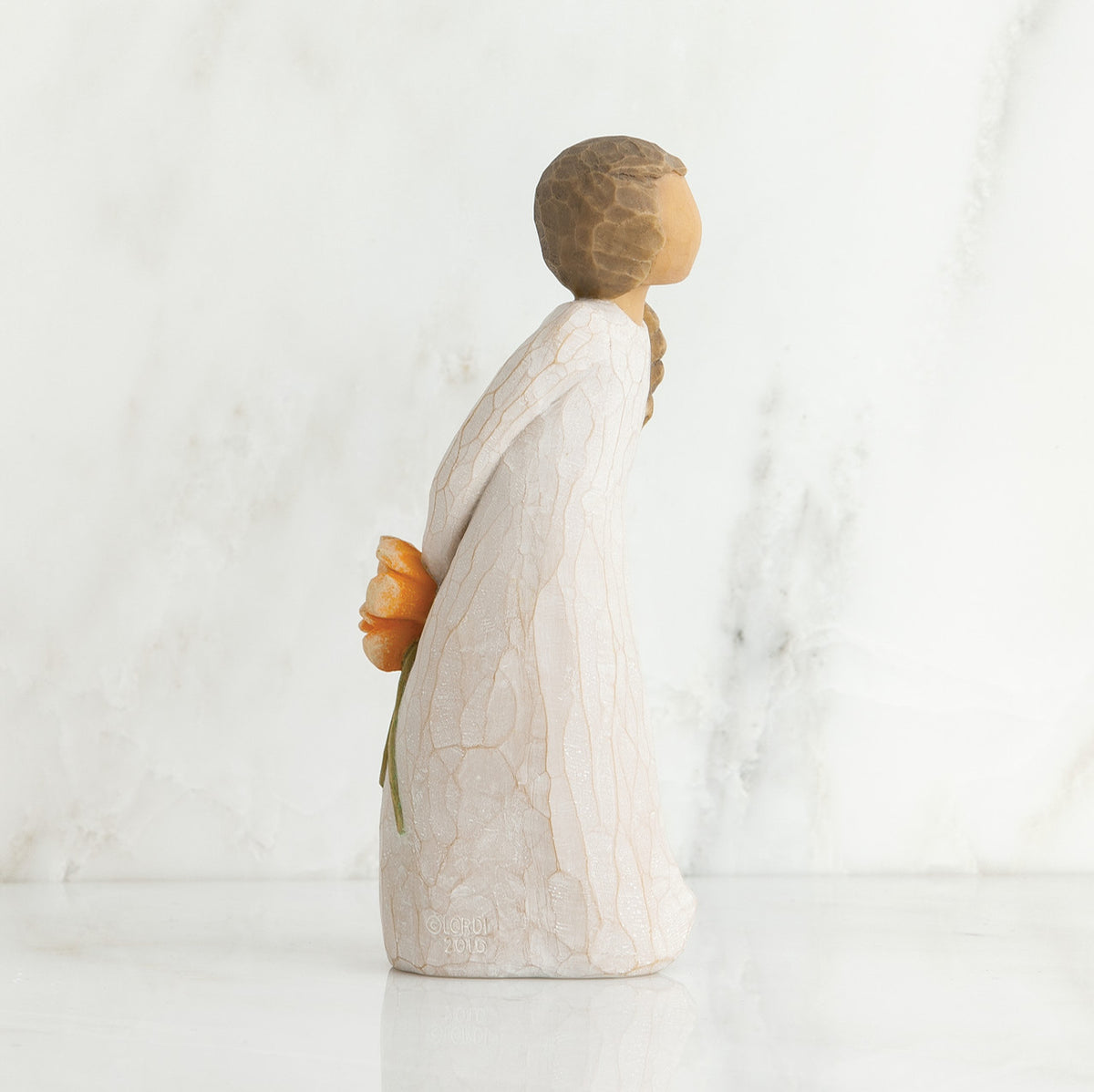 Left side view of girl with brown hair in braid over right shoulder leaning forward as she holds orange flowers behind her back