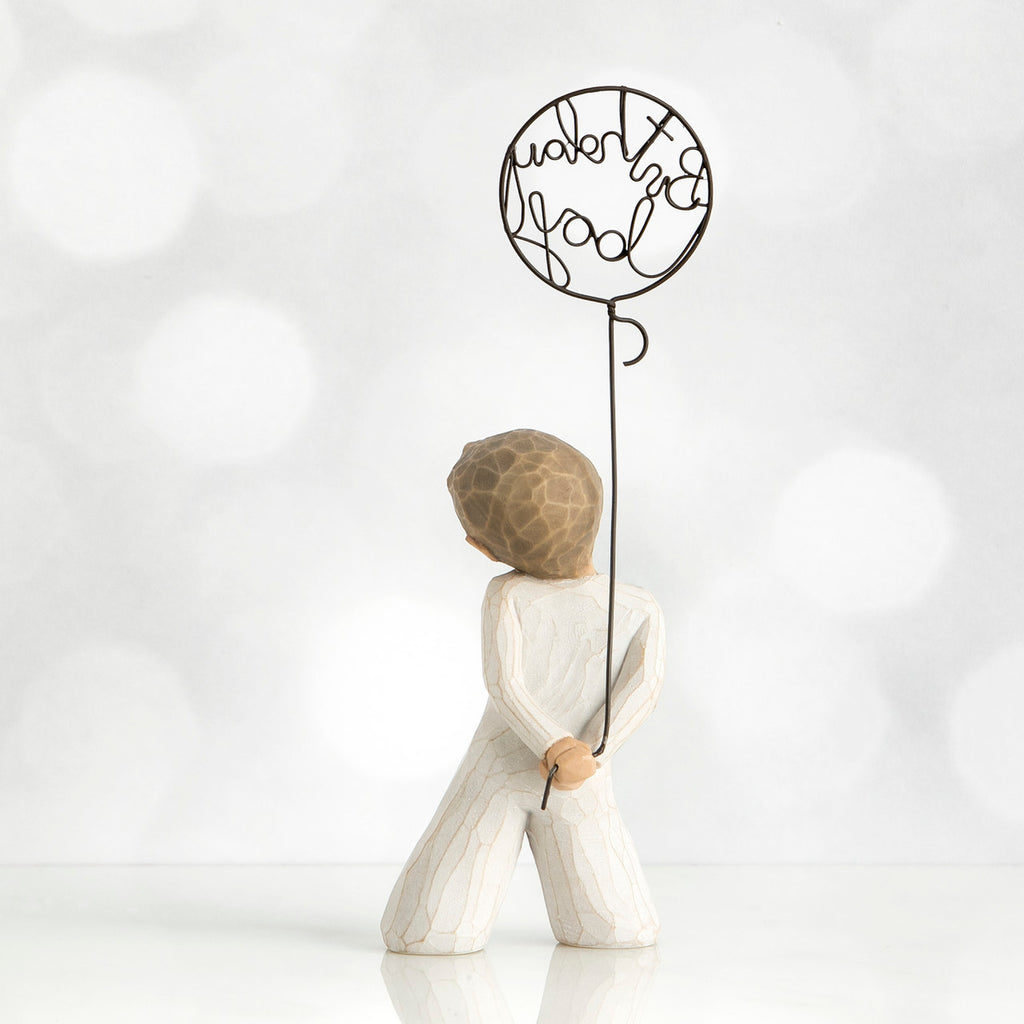 Back view of little boy with light brown hair holding a wire balloon behind his back. Text on balloon is wire