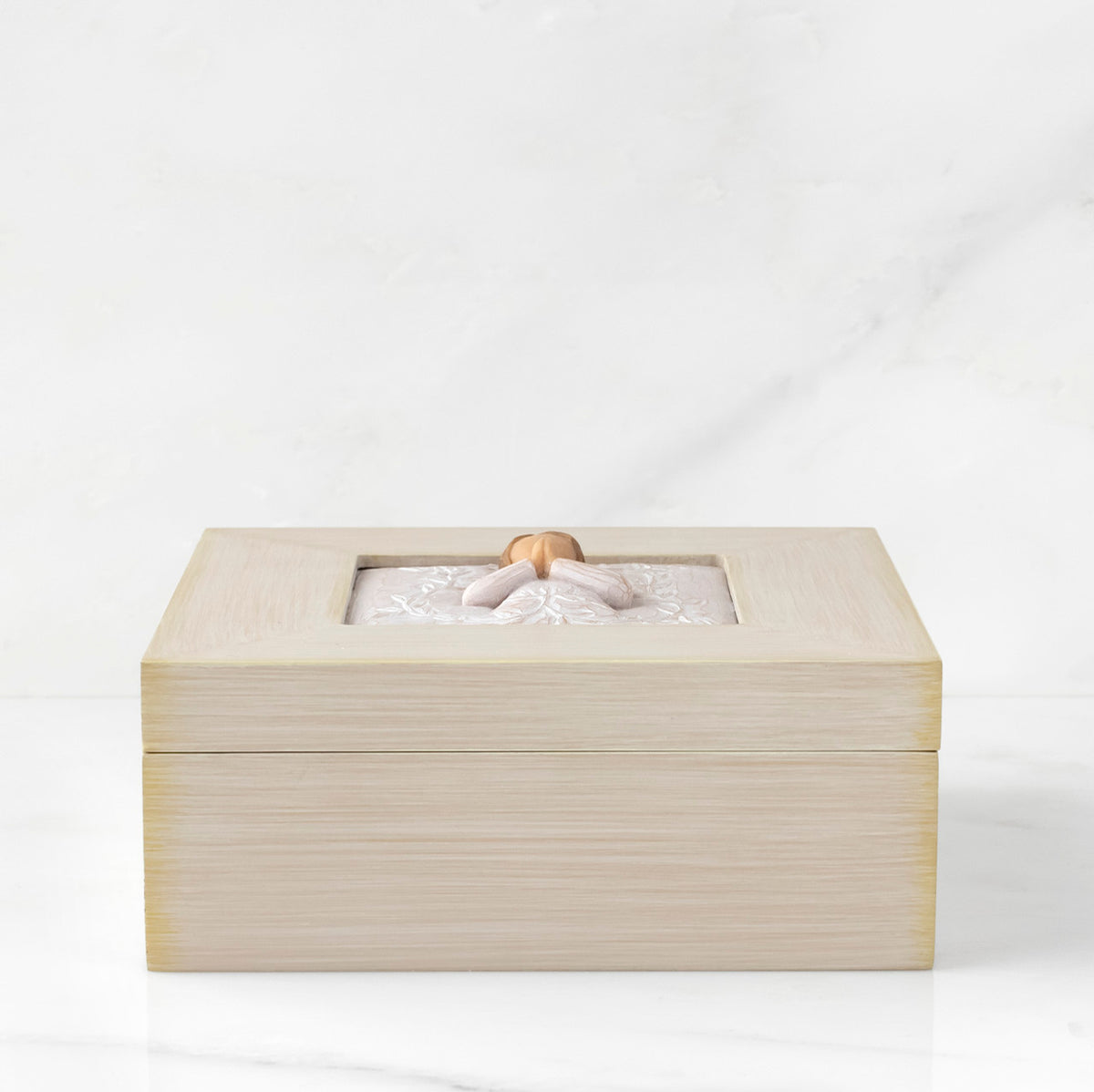 Side View: Cream square wood box with hinged lid, carving on lid of female in cream dress with hands in prayer position, surrounded by leaves and vines