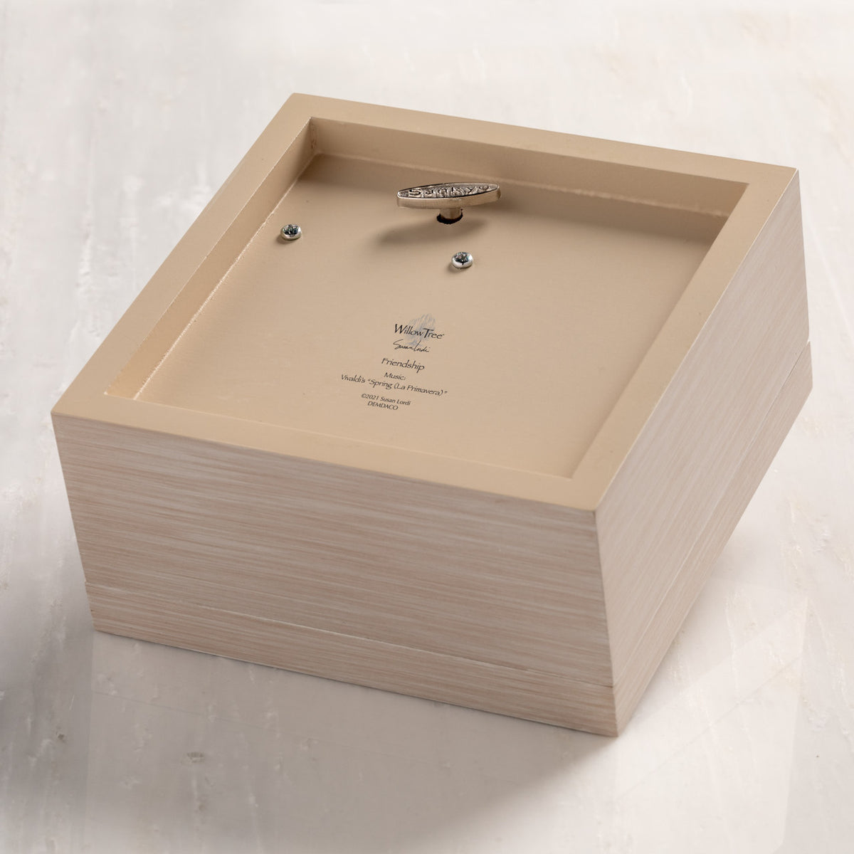 Bottom of cream wood box with hinged lid, showing winding mechanism for music.