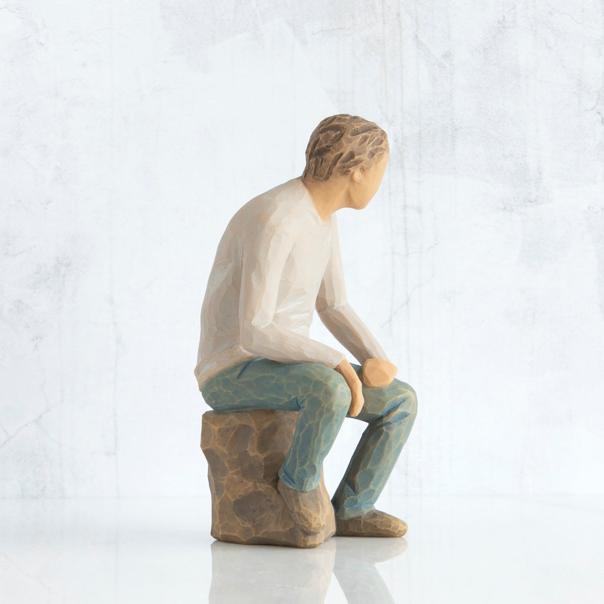 Right-facing view, adult male figure in light gray shirt and blue jeans, seated on gray rock