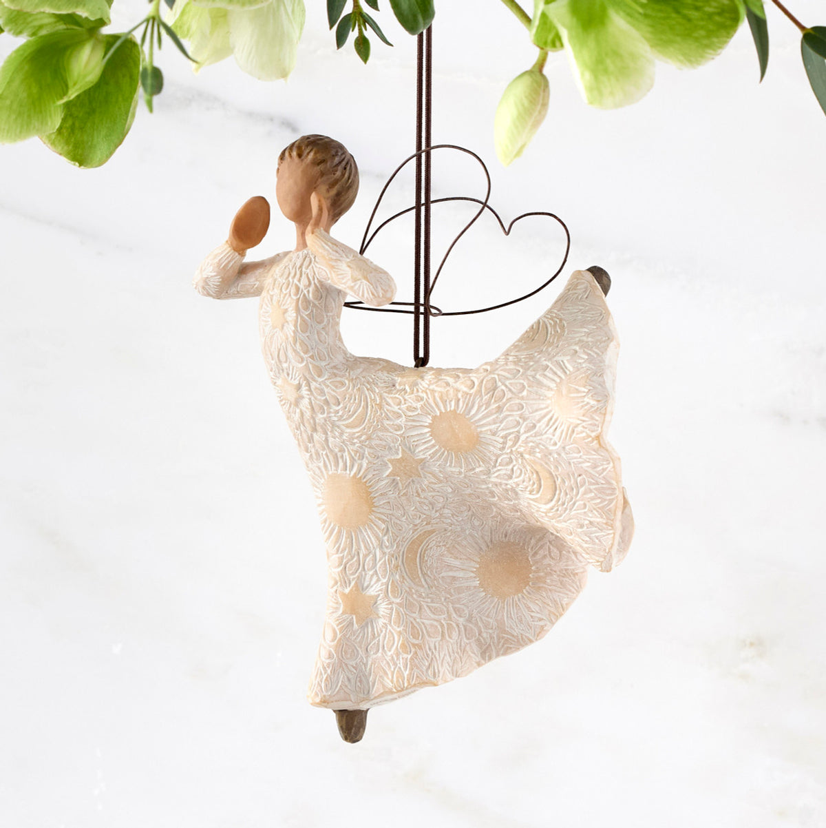 Left view of figure in cream dress carved with celestial patterns in ballet pose with hands raised to mouth and leg up behind her, wire wings on back and ornament hook on head