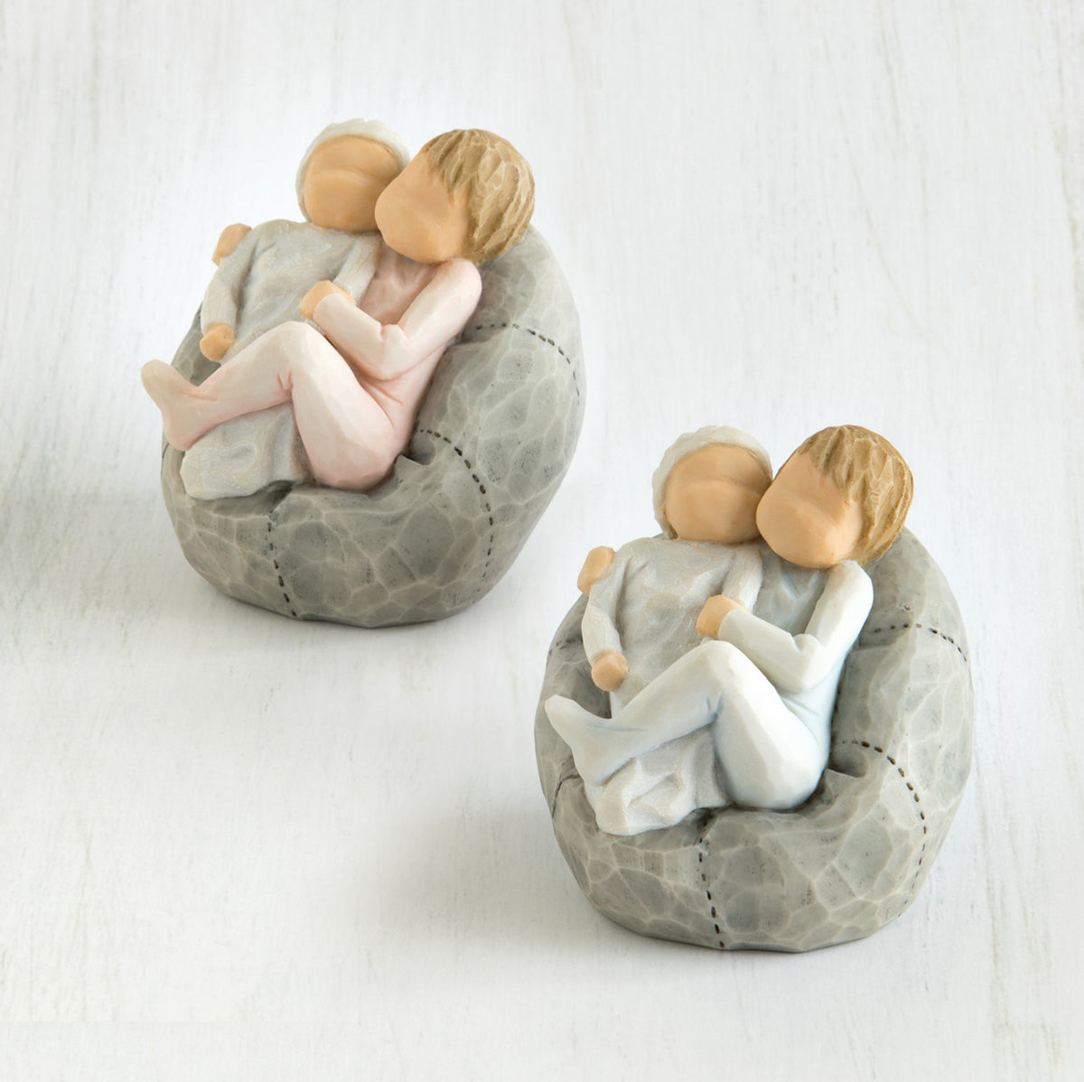 Set of two baby figurines on grey beanbags being held by their older sibling