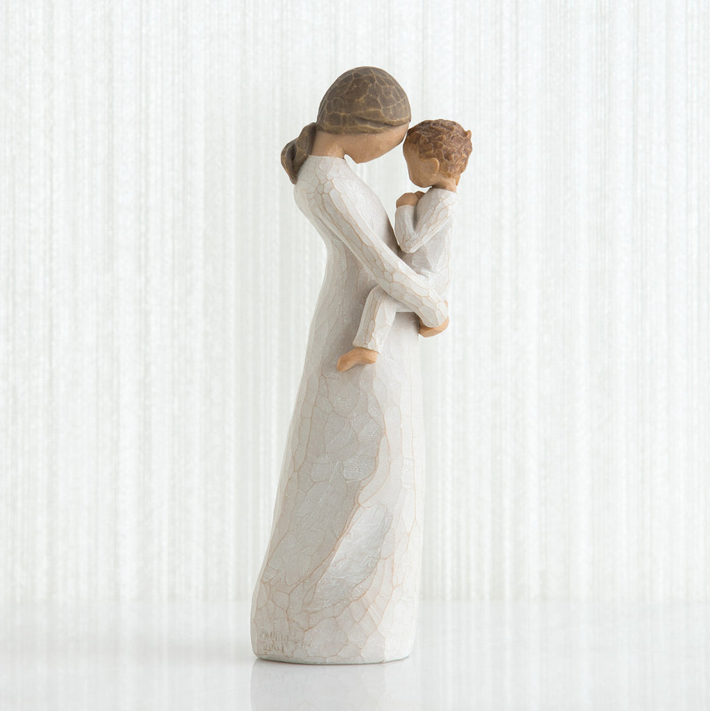Side view of faceless mom figurine wearing white dress holding child in white outfit in her arms