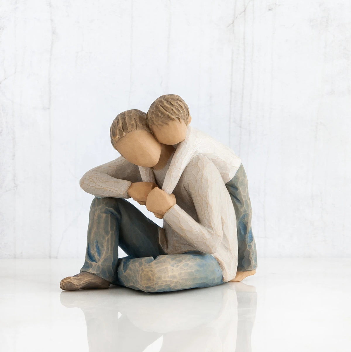 Faceless man figurine sitting with young boy hugging him over his shoulders - wearing white shirts and blue jeans - all white background
