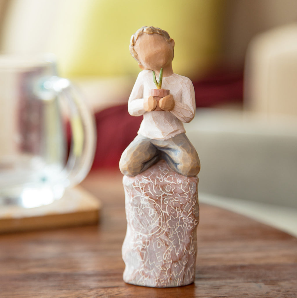 Willow Tree something special, 5.5”h hand-painted figure of small boy holding plant in pot, kneeling on tall rock etched with nature imagery, on desk