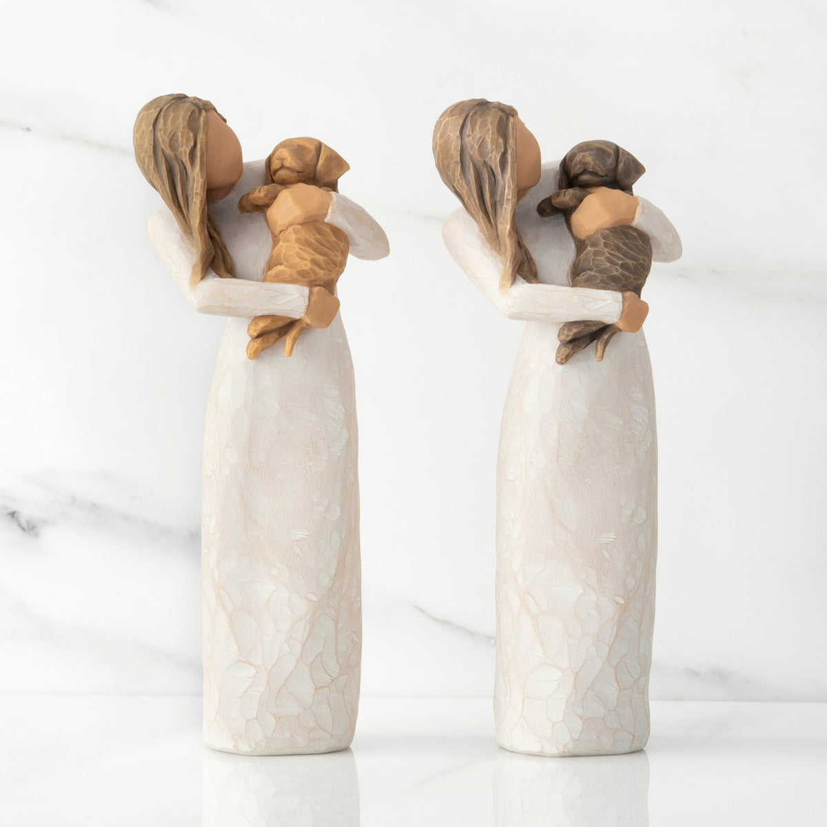 Front views of two standing female figures in cream dress, one holding golden color puppy, the other holding dark color puppy