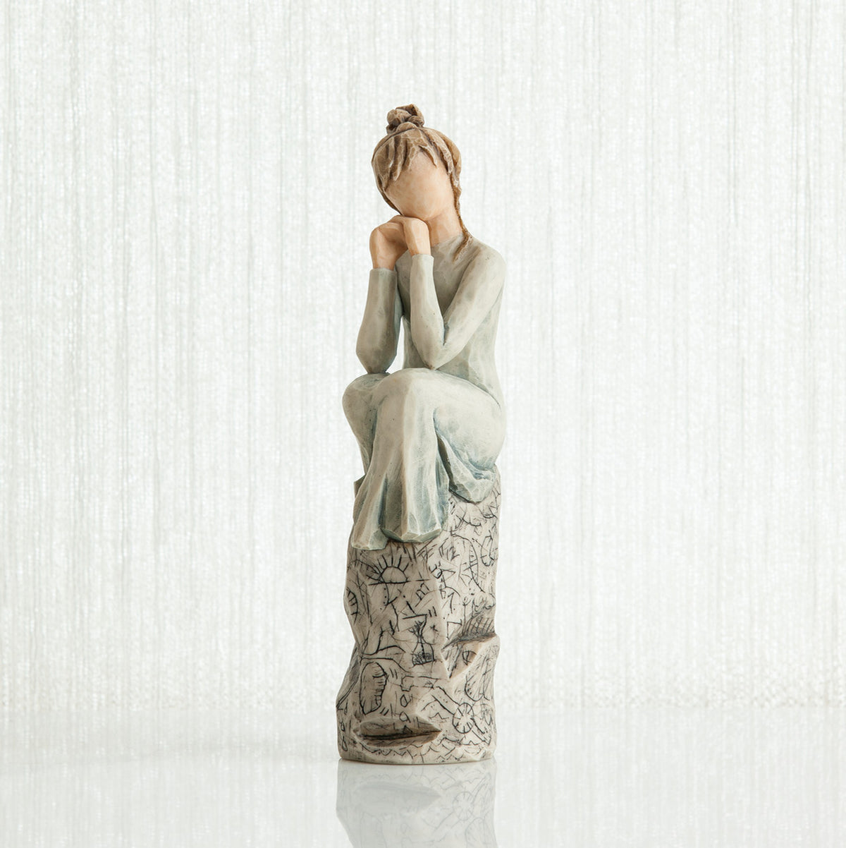 Woman figurine with brown hair in a bun and in white/blue dress sitting on grey printed rock