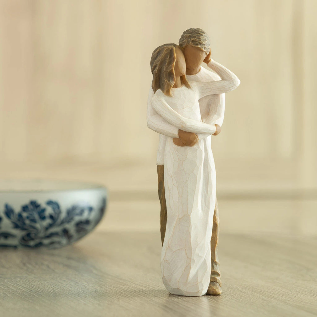 Front view of couple, standing with arms around each other. Woman and man have darker skin tones and hair color. Decorative bowl in background.