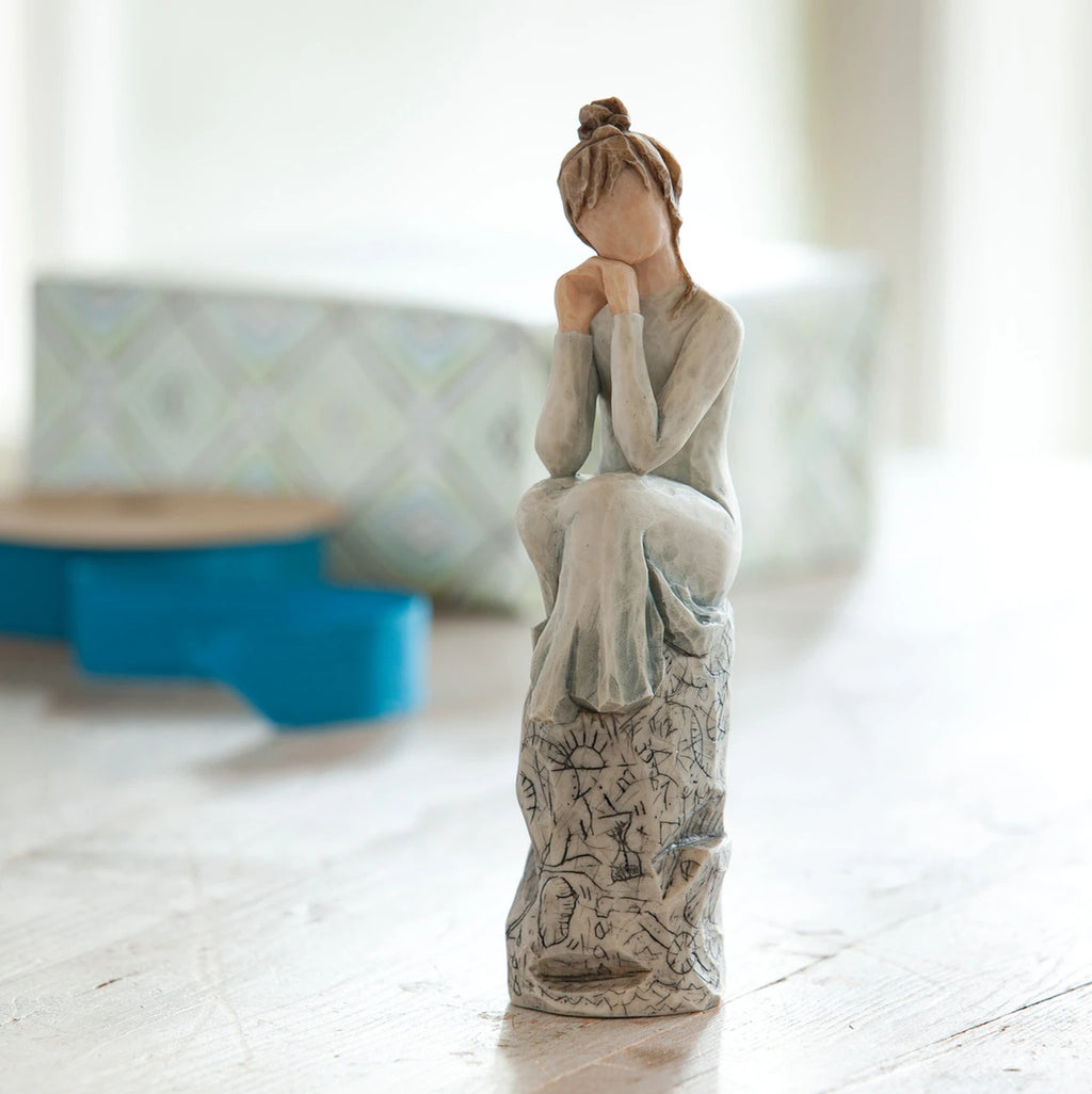 Willow Tree Patience, 7”h hand-painted resin figure in blue/gray dress, hands under chin, sitting on grey rock etched with symbols, on desk by window