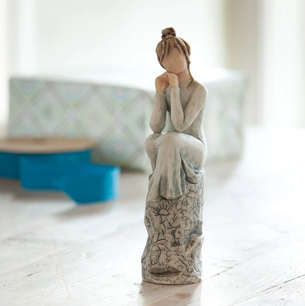 Willow Tree Patience, 7”h hand-painted resin figure in blue/gray dress, hands under chin, sitting on grey rock etched with symbols, on desk by window
