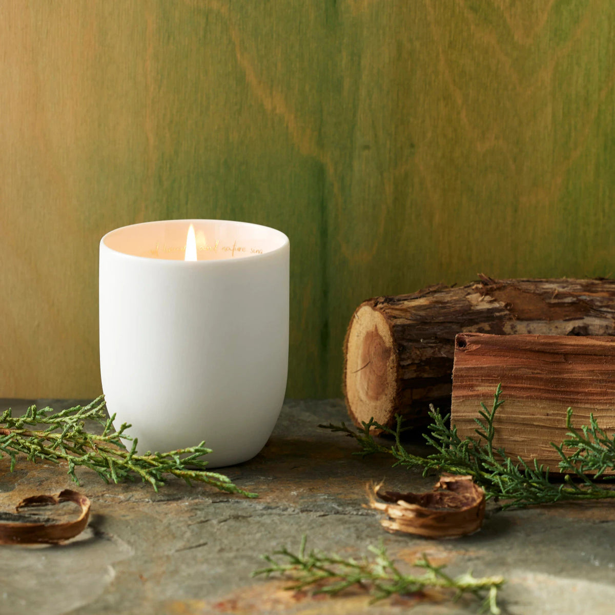 Willow Tree Peaceful Cypress and Cedar Candle, 3.5"h off-white ceramic vessel with plant-based wax and blend of natural oils, "...and heaven and nature sing" sentiment in gold inside rim, in front of deep green painting